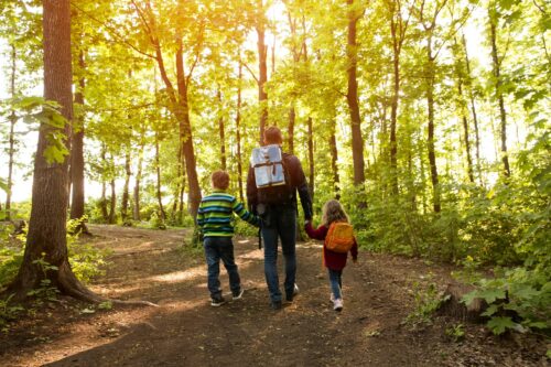 Father and two kids with backpack hiking in forest