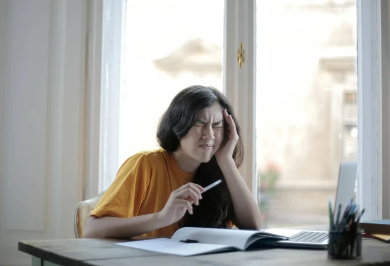 Person holds side of head in pain working at table