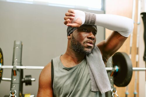 Sportsman wiping off sweat and feeling delayed onset muscle soreness after workout