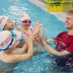 Swimming teacher high fives young swimmers in the pool