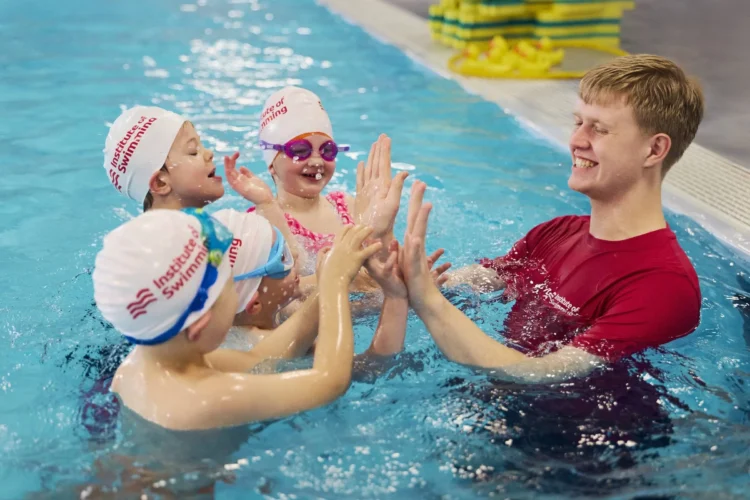 Swimming teacher high fives young swimmers in the pool