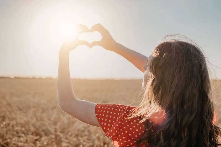 Woman holds hand to sun making love heart sign