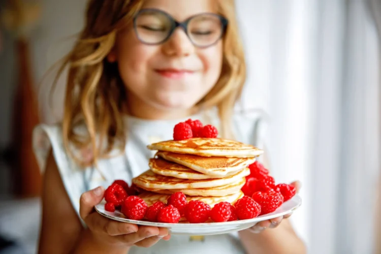 girl with a large stack of pancakes and raspberries