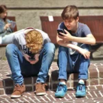 Two youngsters sit on their phones