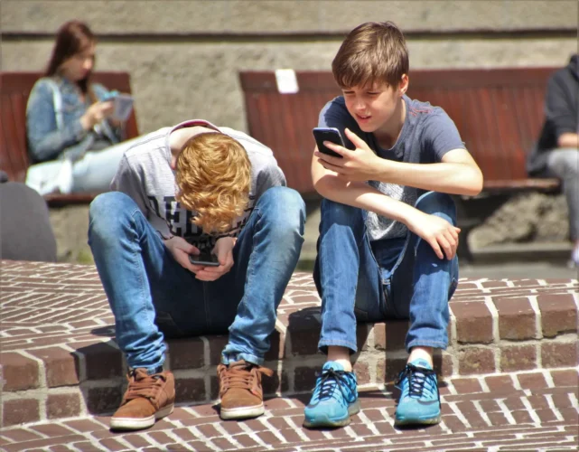 Two youngsters sit on their phones