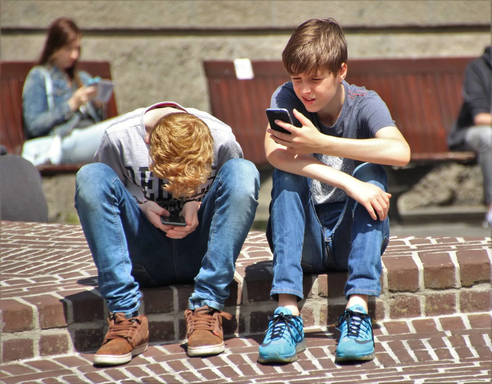Two youngsters sit on their phones