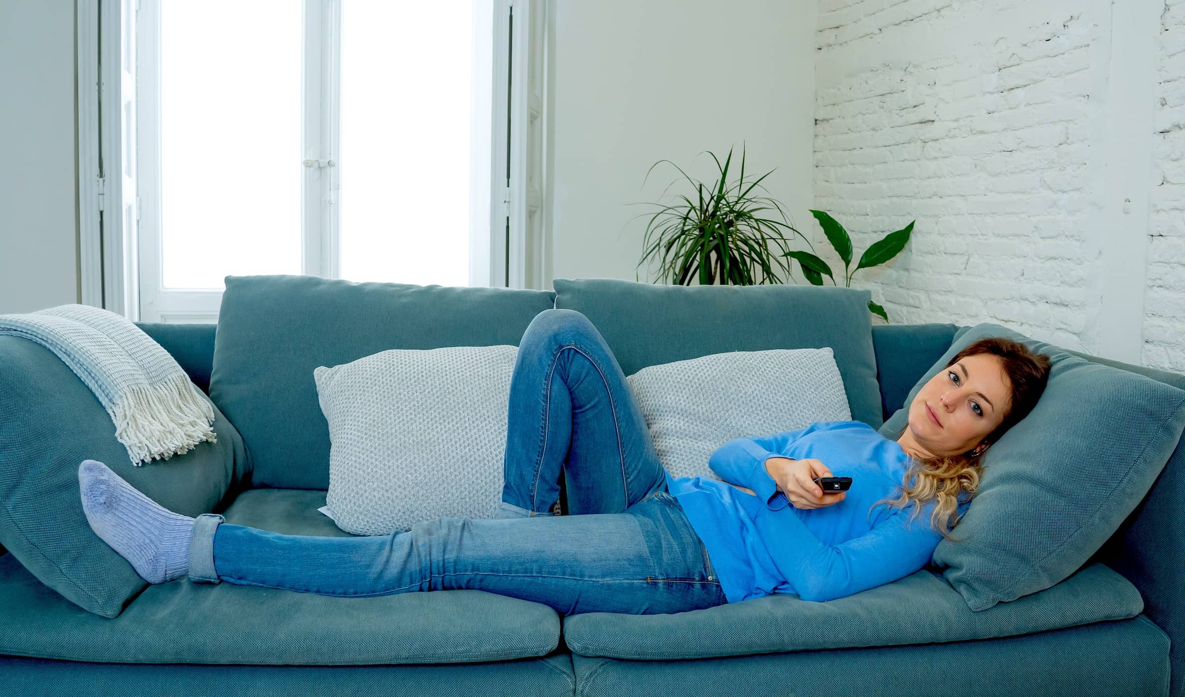 Bored woman watching TV at home changing channels with remote control
