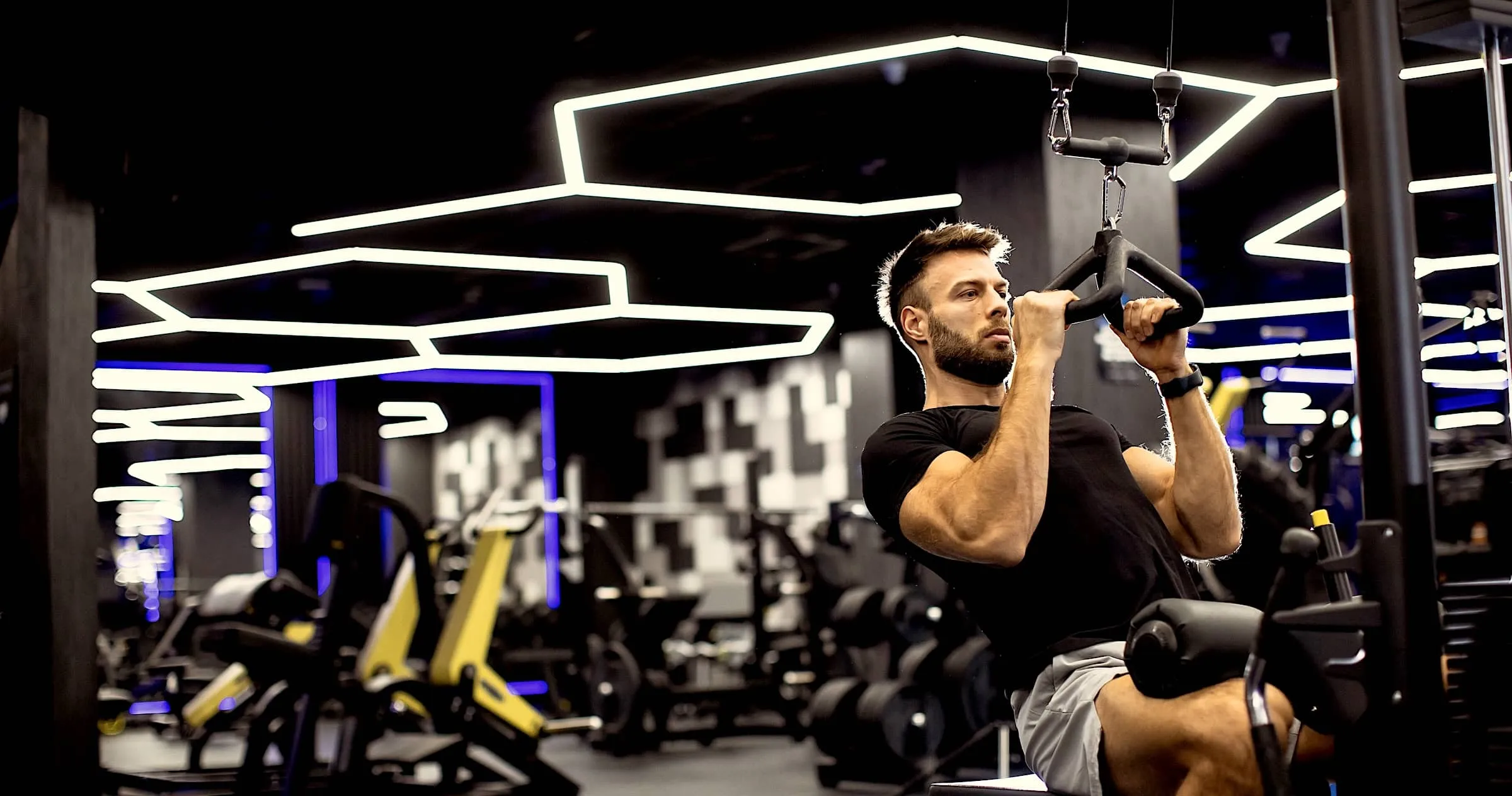 Man exercising on pull-up machine in modern gym with bright neon lights
