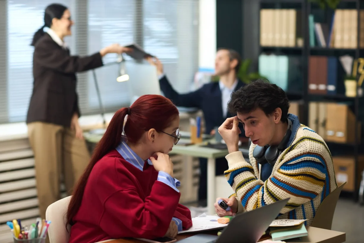 Man holding pen and looking concerned, two middle aged colleagues working in background in modern office