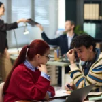 Man holding pen and looking concerned, two middle aged colleagues working in background in modern office