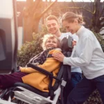 Two helpers picking up disabled senior woman for transport
