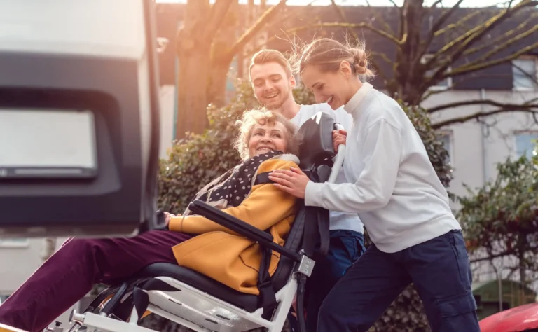 Two helpers picking up disabled senior woman for transport