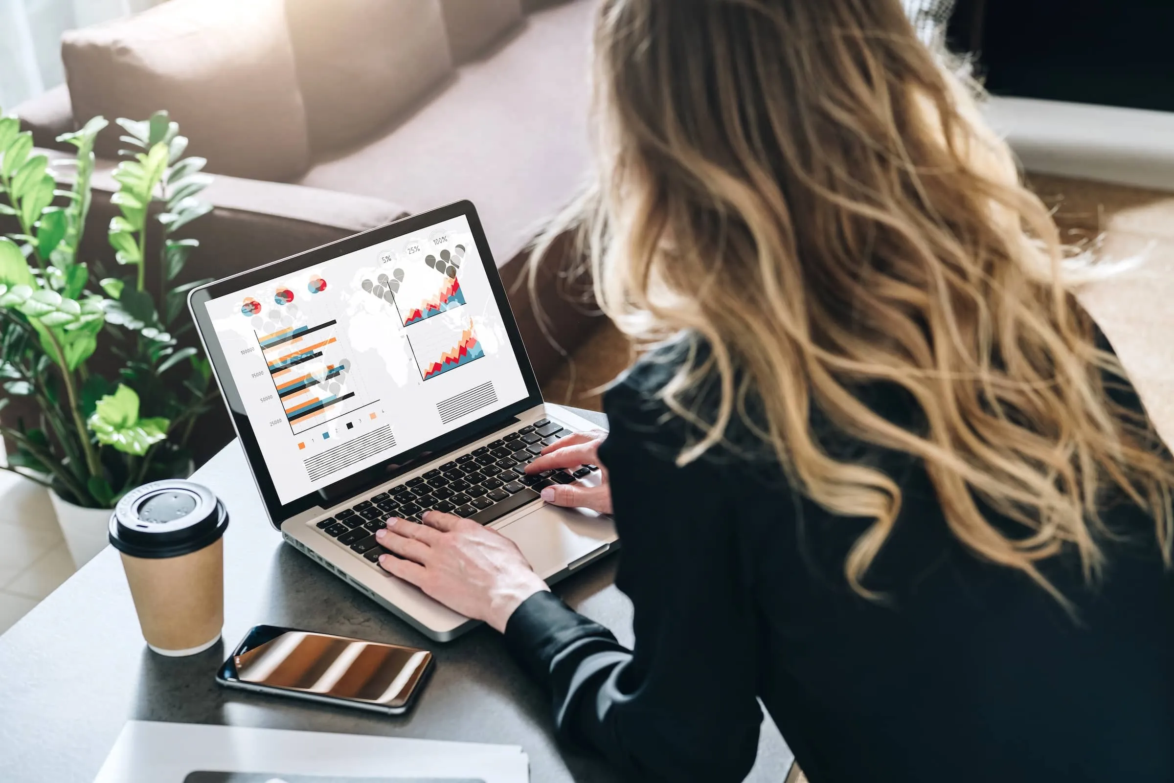 Businesswoman is sitting at table, working on laptop with graphs, charts, diagrams, schedules on screen