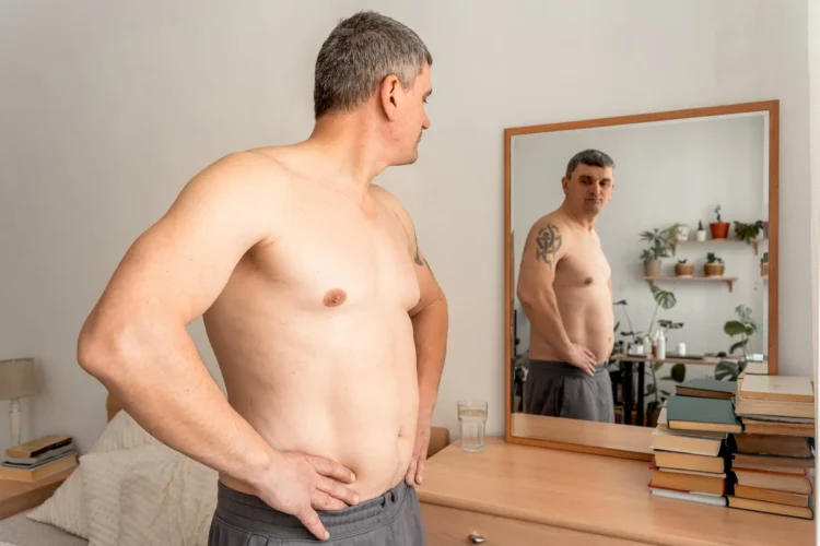 Mature man standing shirtless, looking at his reflection in a mirror