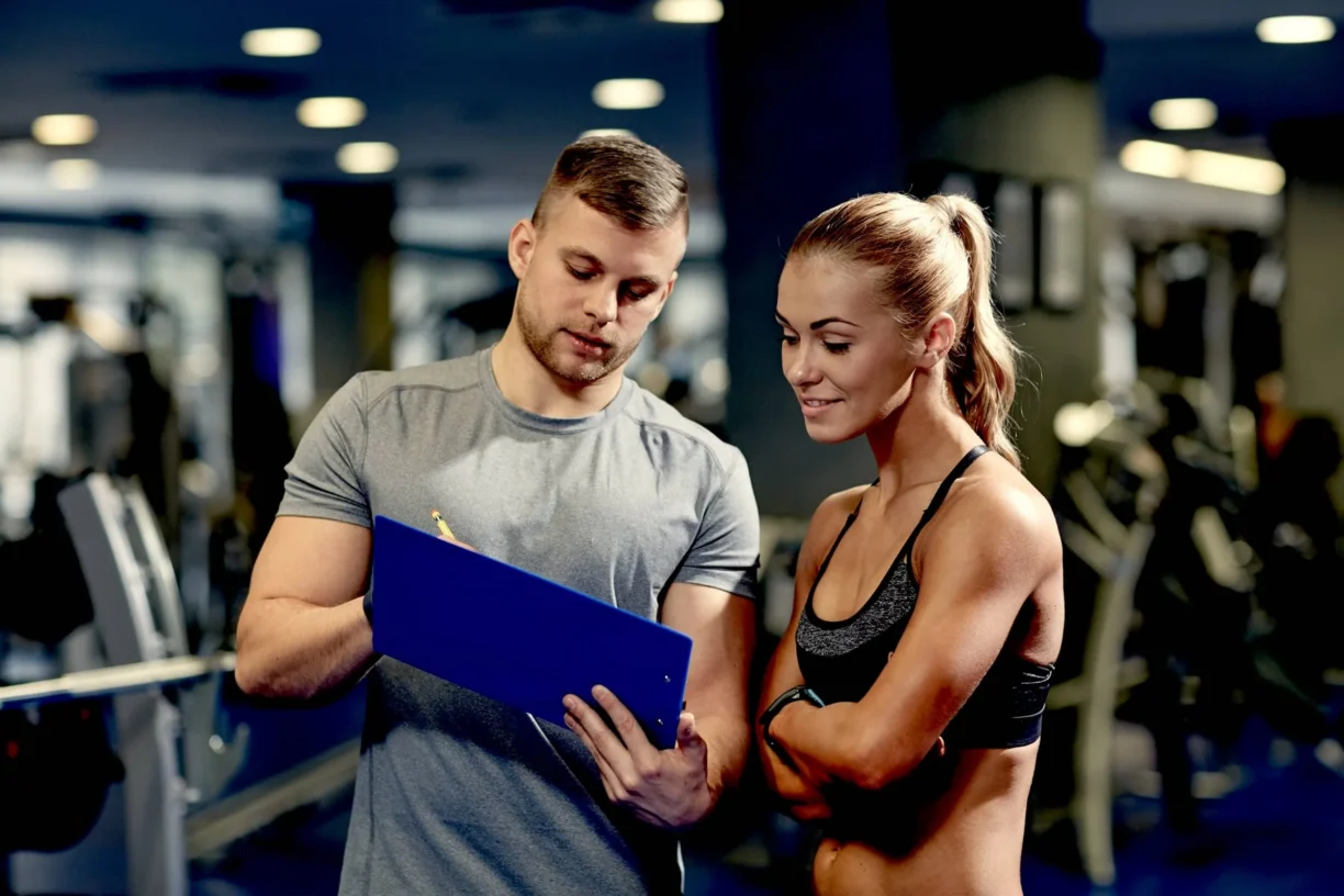 Smiling young woman with personal trainer in gym