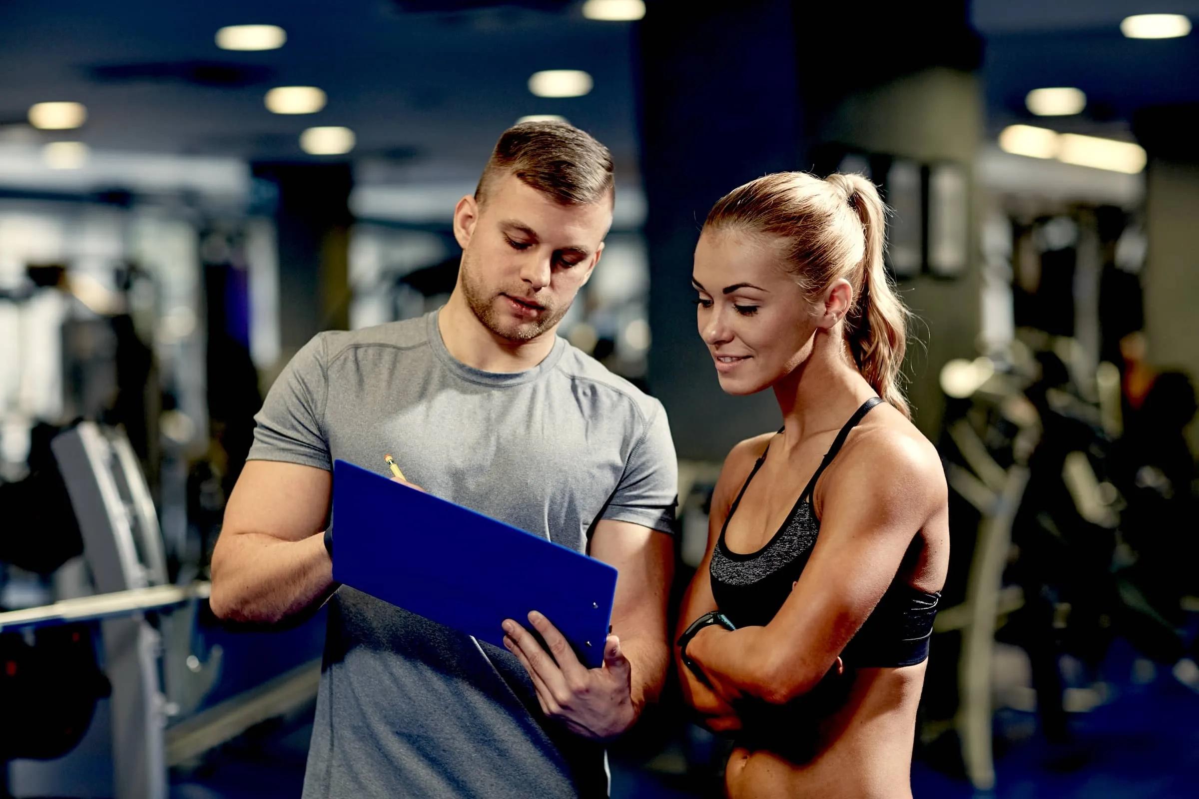 Smiling young woman with personal trainer in gym