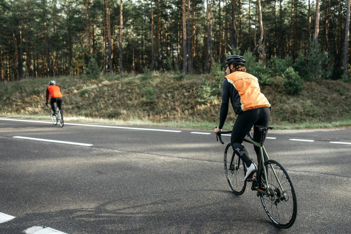 Two cyclists wearing reflective vests riding on a forest road