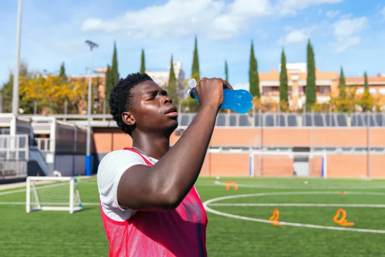 athlete drinking energy sports drink on a football pitch during training session