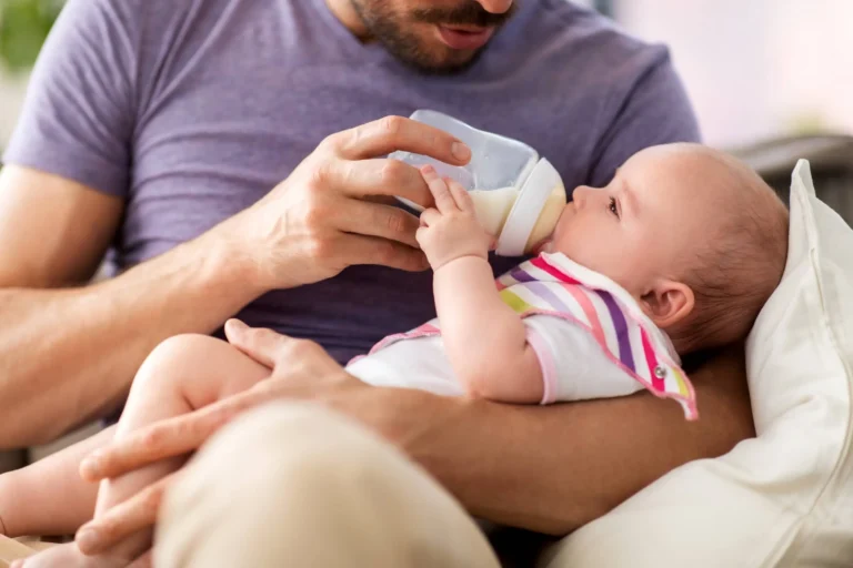 Father feeding little daughter with baby formula from bottle