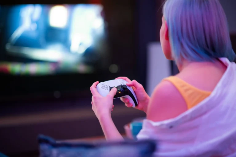 Girl with colorful blue and pink hair hold joystick and play video games at home at night