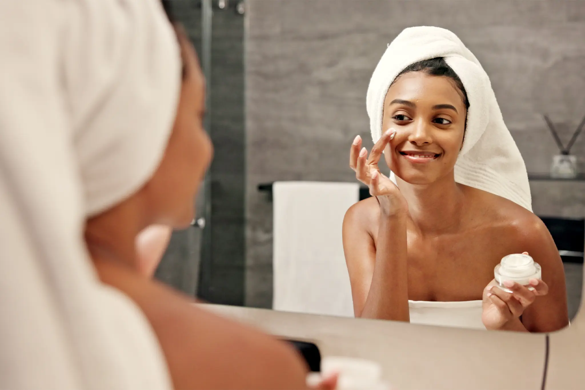 Person applies skin cream to face in mirror