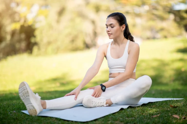 A woman in white athletic wear gently stretches on a yoga mat in the park