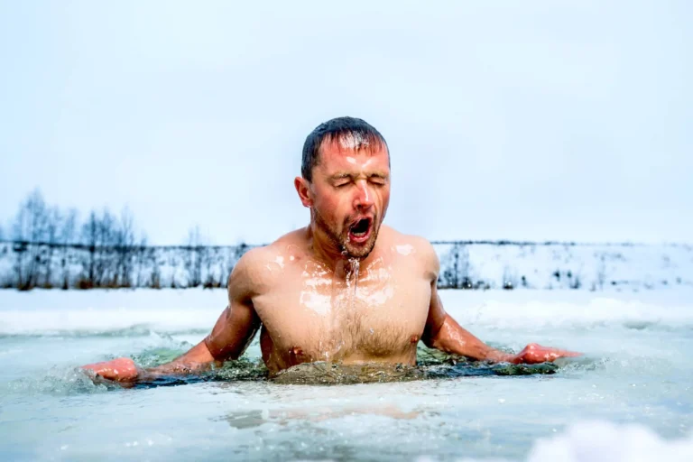 Young man swimming in the winter lake in the ice hole