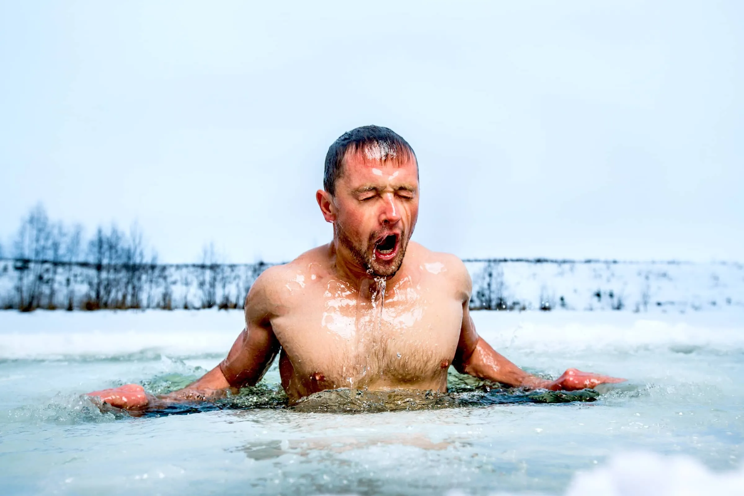 Young man swimming in the winter lake in the ice hole