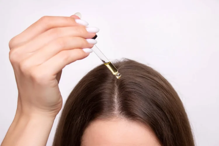 A young woman applies a drop of oil from a pipette to her scalp