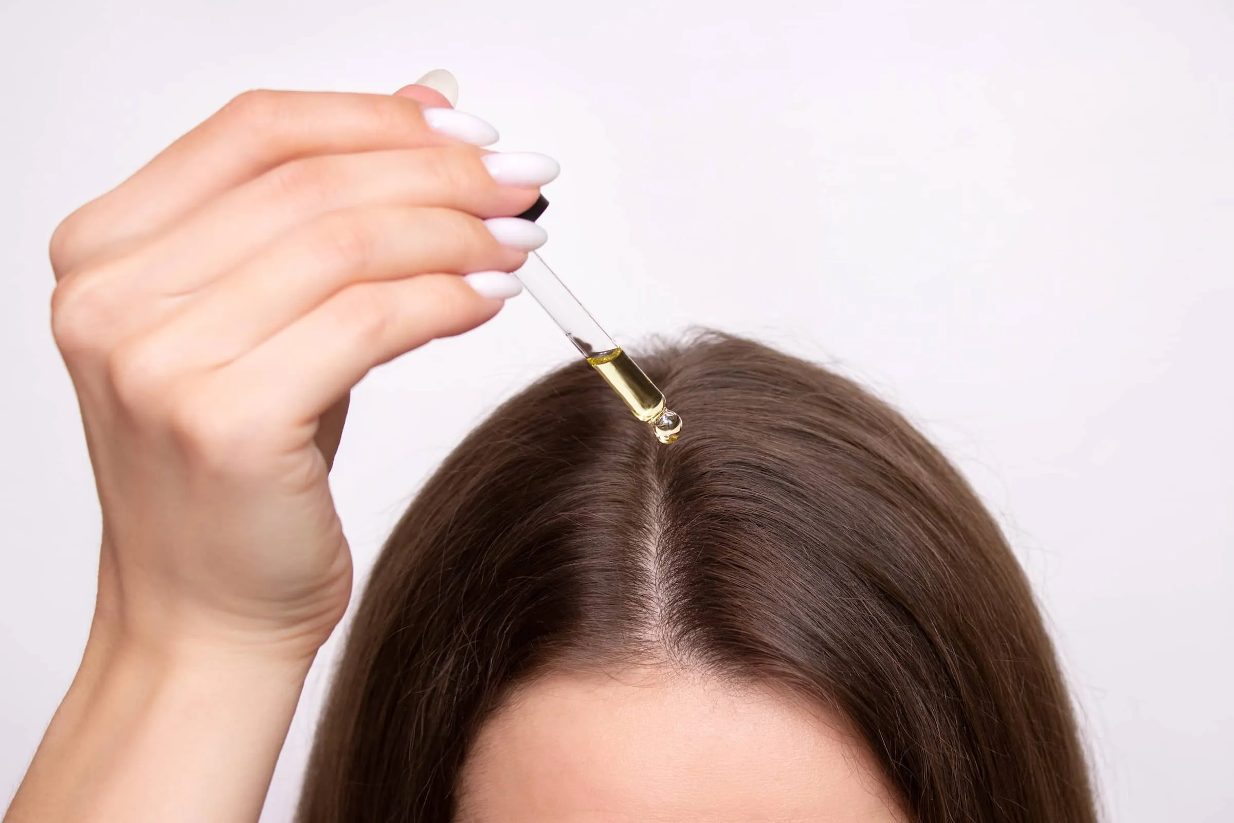 A young woman applies a drop of oil from a pipette to her scalp