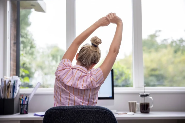 Woman Working From Home On Computer In Home Office Stretching At Desk